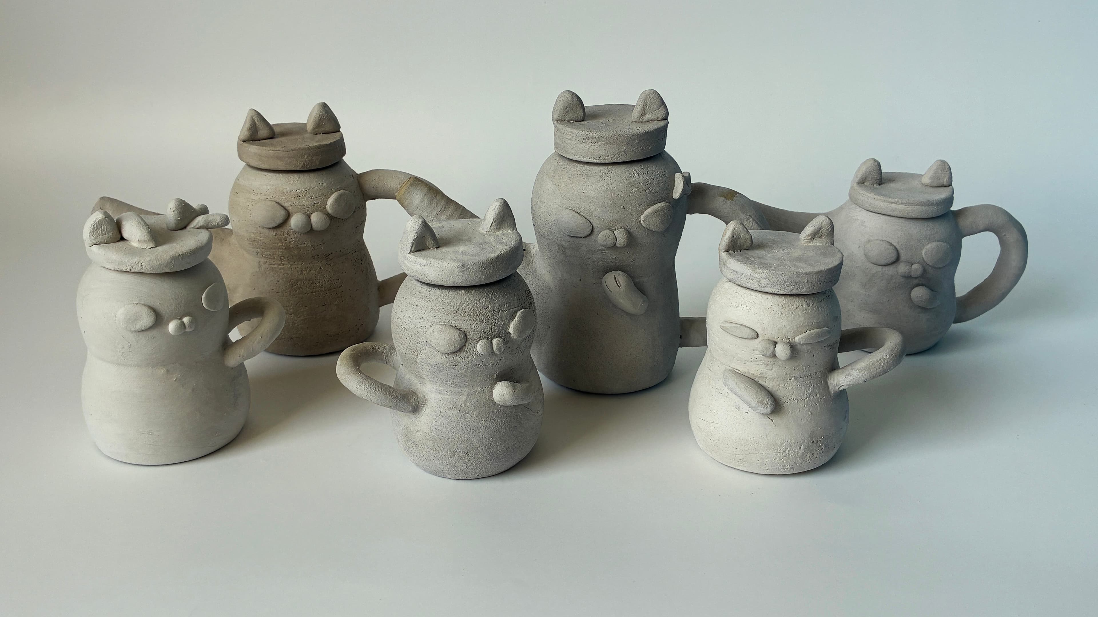 Handmade ceramic teapots with animal-shaped lids arranged in a studio display.